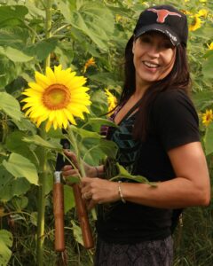 Stacy Thomas holds a sunflower and a pair of shears in her hand, smiling at the camera.
