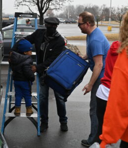 man holds boy on ladder while another man lifts a suitcase