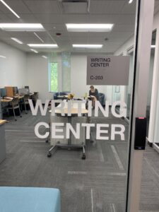 Glass door with the words "writing center C-203" on it. The room is in the back ground of the photo.