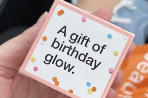 A box with confetti that reads "a gift of birthday glow."