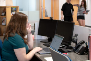Liz Hartig on laptop with students in the background.